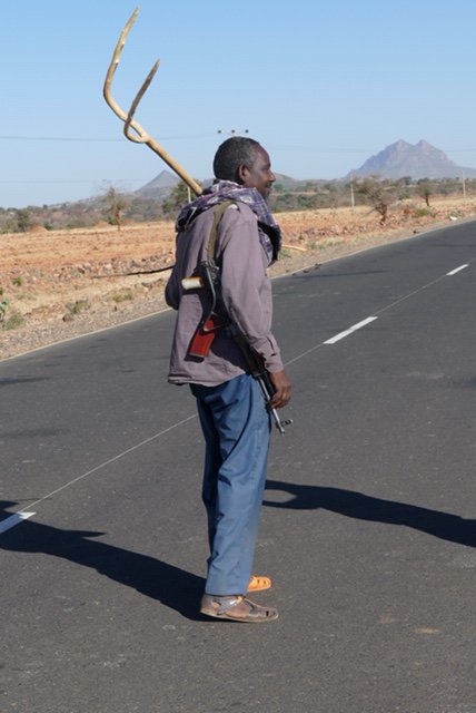 Man on road with gun and pitchfork - note his shoes